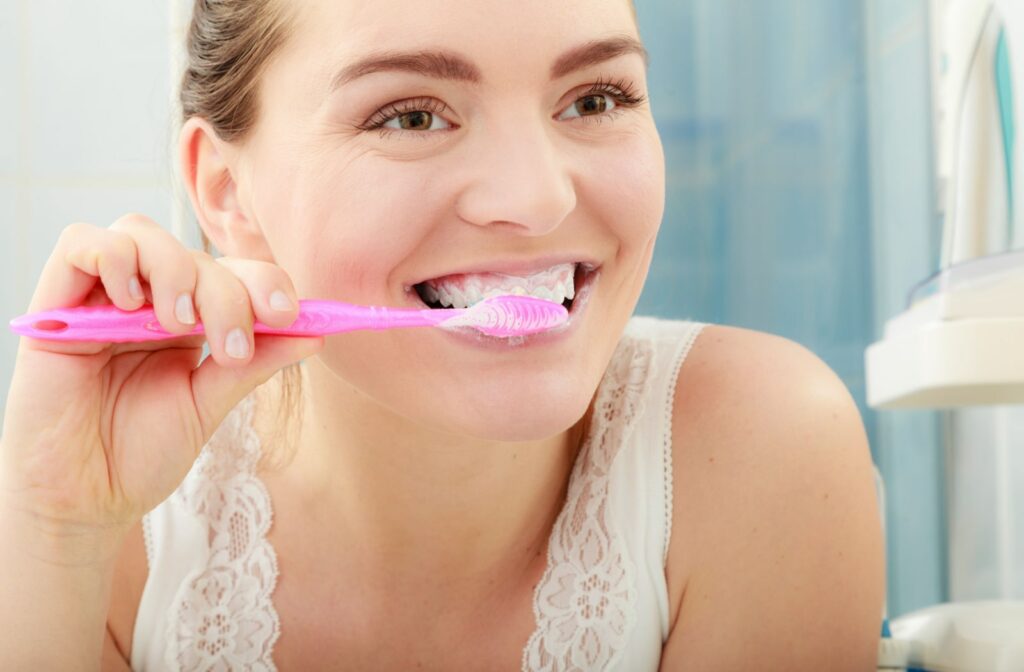 A close-up of a woman in a mirror brushing her teeth with a whitening toothpaste