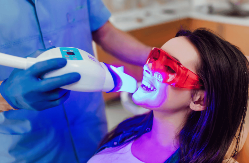 A young woman is undergoing a teeth whitening procedure, the dentist is bleaching her teeth and uses a UV light