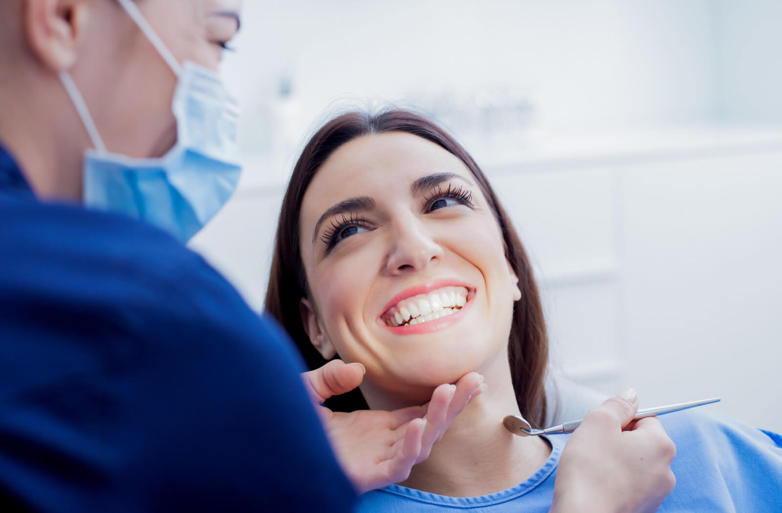 A woman sitting in a dentist's chair smiling while her dentist examines her teeth.