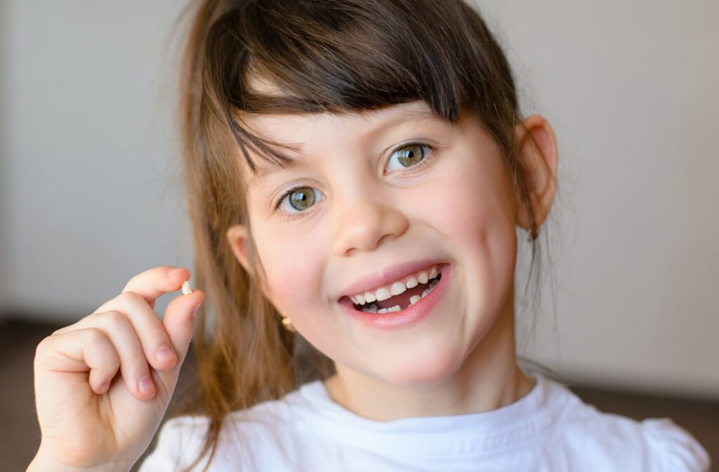 A young girl holds her first lost tooth in her hand while she smiles