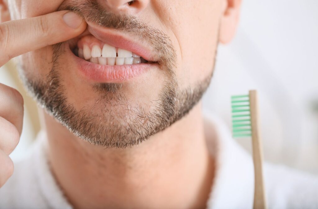 A man brushing his teeth lifts his lip up to expose his gums.