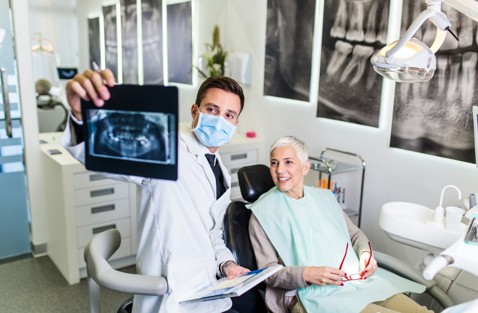 A dentist holding up an X-ray and showing it to a female patient as she sits in the dental chair