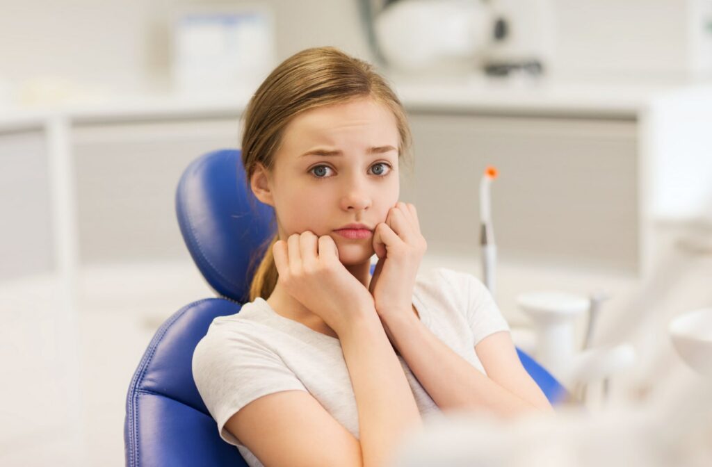 A young girl sitting in a chair at the dentist's office with an anxious look.