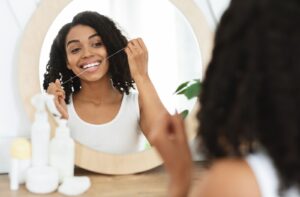 A young woman looking in the mirror and flossing while smiling