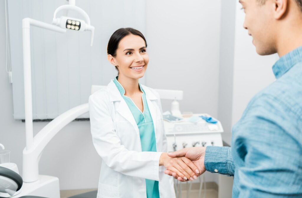 A female dentist looking at her patient and smiling while shaking his hand