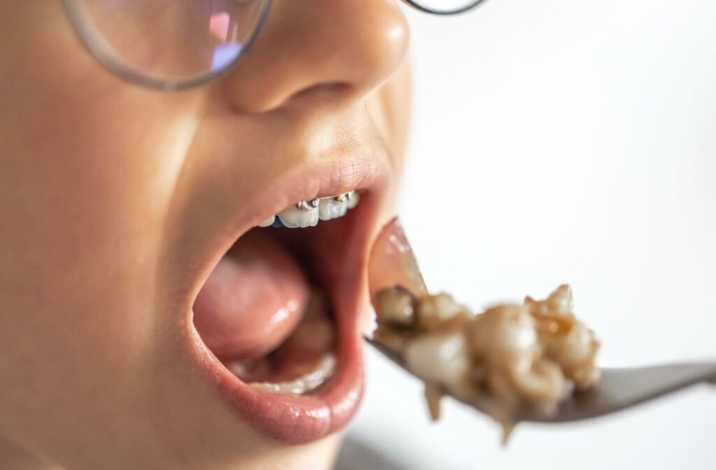 A young girl with braces eats a forkful of oatmeal and fruit.