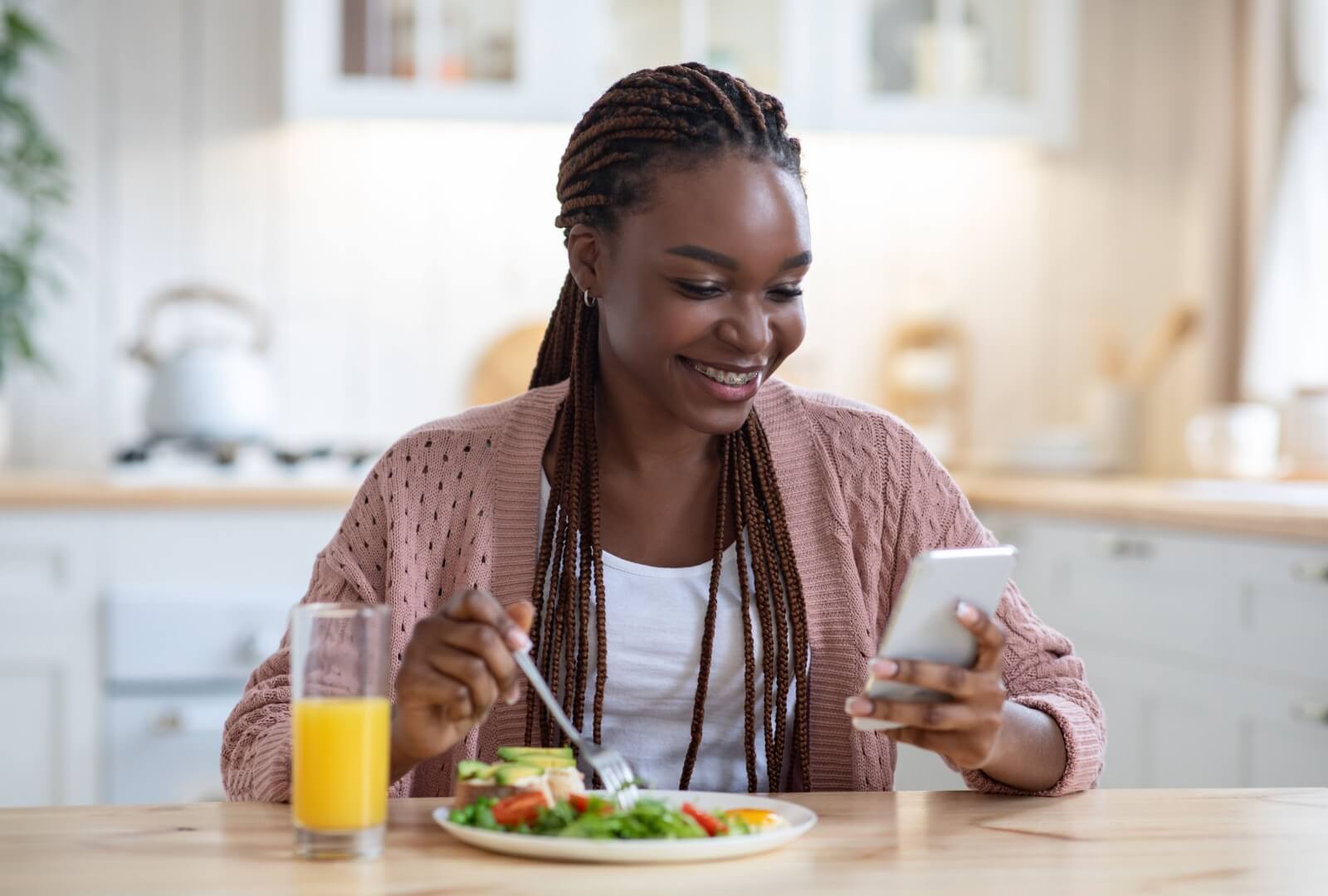 A young woman looking up on her phone what foods are safe to eat with her new braces while enjoying a salad.