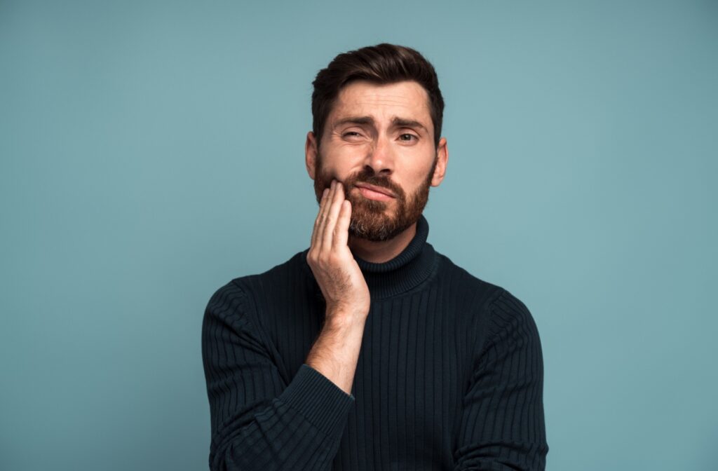 A man touching the side of his face because he has tooth pain.