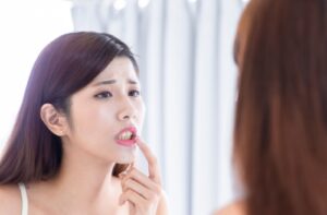A young adult frowning while examining their yellow teeth in a mirror.