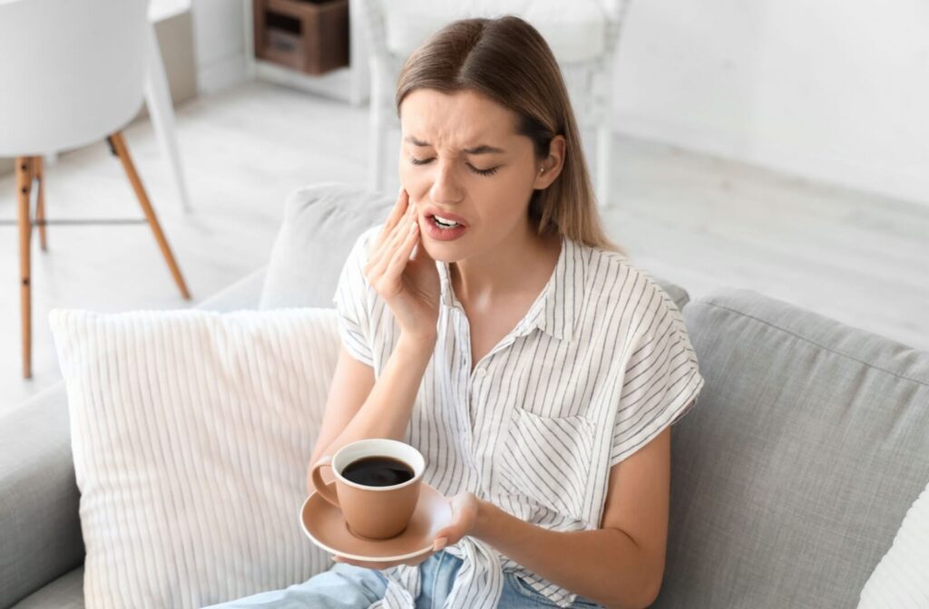 Person experiencing tooth sensitivity while drinking a hot beverage.