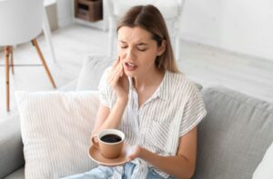 Person experiencing tooth sensitivity while drinking a hot beverage.